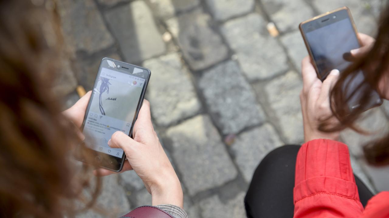 Bilden föreställer två personer som håller i varsin mobiltelefon.